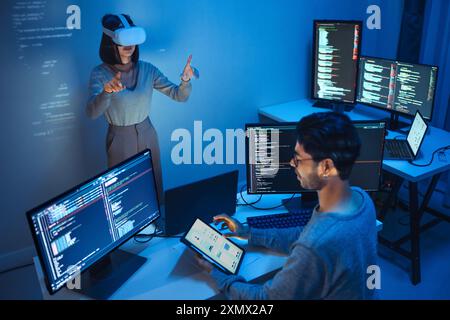 developer uses a VR headset to interact with projected interface designs, while colleagues discuss and code on screens, highlighting the integration o Stock Photo