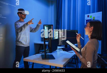 Asian UX designer works on a tablet while a colleague tests a VR application ,integration of user experience design and virtual reality development in Stock Photo