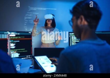 developer uses a VR headset to interact with projected interface designs, while colleagues discuss and code on screens, highlighting the integration o Stock Photo
