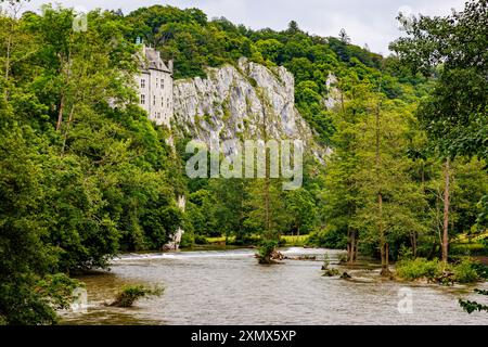 Rocky mountain, part of Walzin Castle protruding from lush green trees and Lesse river, abundant green vegetation in background, overflowing stream, c Stock Photo