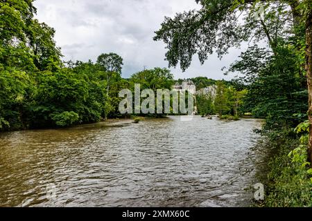 River Lesse with Walzin Castle on a rocky hill in background, stream overflowing lightly with lots of water between abundant green leafed trees, cloud Stock Photo