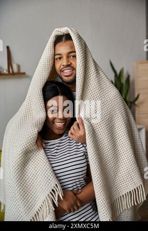 A loving African American couple shares a playful moment under a blanket at home. Stock Photo