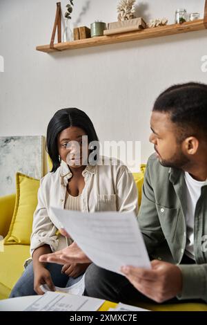 An African American couple reviews paperwork while sitting on a yellow couch. Stock Photo