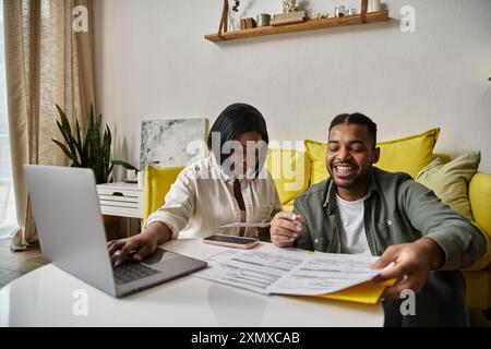 An African American couple sits at a table together, looking at paperwork and smiling. Stock Photo