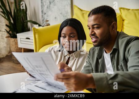 An African American couple sits on a couch, reviewing paperwork together. Stock Photo