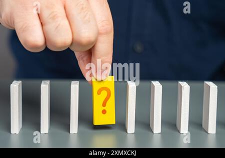 A man studies an unknown element of a chain of processes in the form of dominoes. Finding an answer to a question. Mistake correction. The fact remain Stock Photo