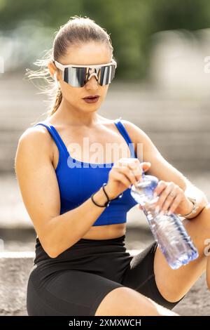 Young sporty woman drinking water from a bottle after exercising at the park. Stock Photo