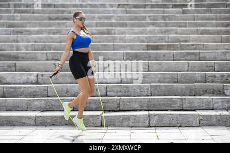 Outdoor shot of woman in sportswear exercising with skipping rope outdoors in a park. Fitness female working out with jump rope in a park. Stock Photo