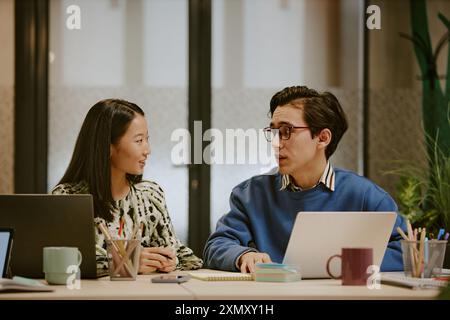 Young ethnically diverse gen Z male and female managers having conversation while working on laptops in modern office Stock Photo