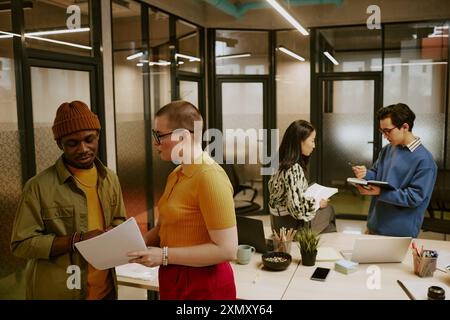 Multi-ethnic group of young men and women wearing stylish casual clothes working in pairs in modern office Stock Photo