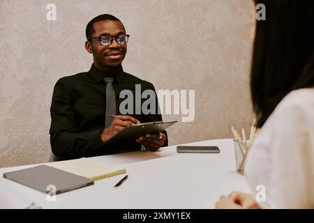 Over shoulder shot of young HR manager making notes while conducting interview with female employee Stock Photo