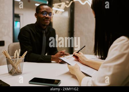 Unrecognizable HR manager making notes in document while interviewing young African American specialist Stock Photo