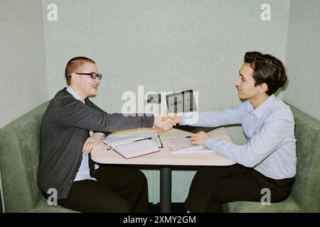 Flash shot of two male and female coworkers sitting in front of each other in modern office doing handshake Stock Photo