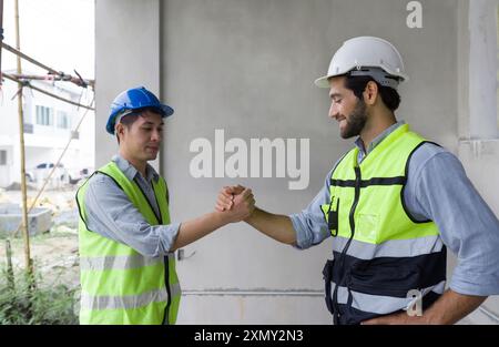 Two construction workers in safety vest and helmet join hands together on a construction site, showing teamwork and agreement. Stock Photo