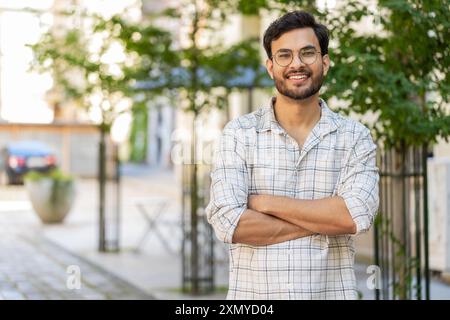 Portrait of happy smiling Indian young man looking at camera, resting, relaxation feel satisfied glad expression of good news outdoors. Hispanic guy tourist on urban city street. Town lifestyles. Stock Photo