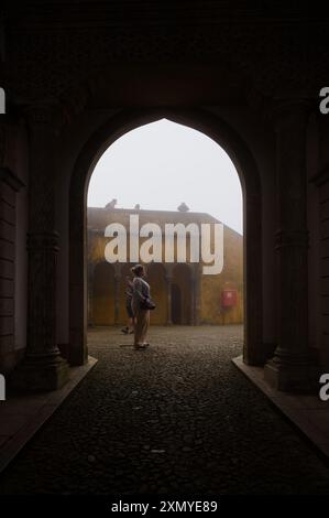 A visitor stands framed by an archway, gazing into the misty courtyard of Pena Palace Stock Photo