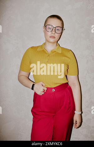 Vertical medium long shot of confident Caucasian woman with buzz cut wearing yellow top and red pants posing for camera Stock Photo