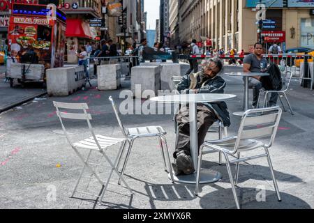 New York, USA - June 8, 2019: A man sits quietly at a table while the city bustles around him. Stock Photo