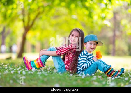 Happy kids boy and girl in rain rubber boots playing outside in the green park with blooming field of daisy flowers Stock Photo