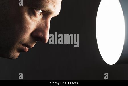 Close up profile portrait of young man staring at the light source over black background, low key studio photo Stock Photo