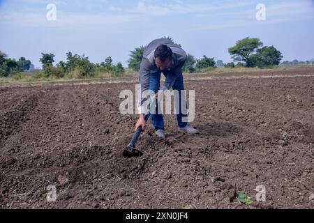 Indian farmer digging his field with a spade, farm and sky background ...