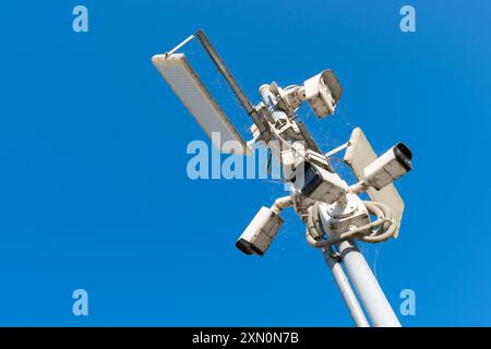 A cluster of surveillance cameras is installed on a pole against a bright blue sky, capturing the surrounding environment in clear daylight. Stock Photo