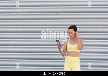 front view of sporty woman holding a phone and wearing earphones while preparing for exercise outdoors Stock Photo