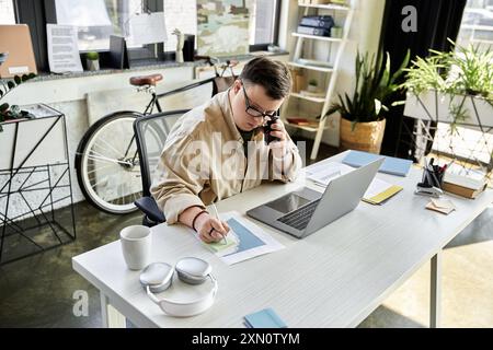 A young man with Down syndrome is on the phone at his desk, working on a graph. Stock Photo