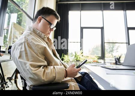 A young man with Down syndrome sits in an office chair, using his smartphone. Stock Photo