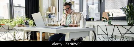 A young man with Down syndrome sits at a desk, working on his laptop. Stock Photo