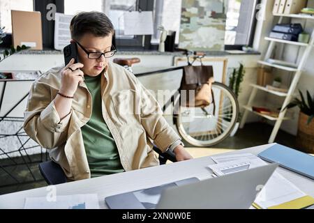 A young man with Down syndrome is on the phone while working at a desk. Stock Photo