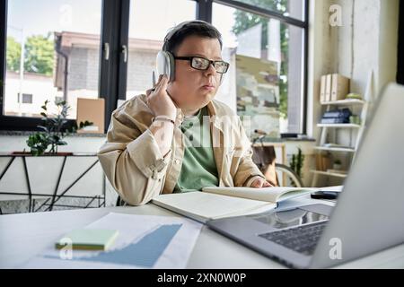 A young man with Down syndrome working on laptop with headphones and notebook Stock Photo