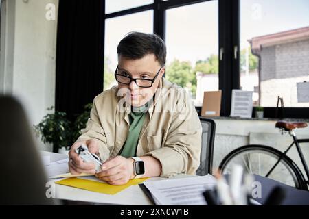 A young man with Down syndrome sits at a desk, working on a task. Stock Photo