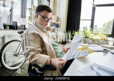 A young man with Down syndrome sits at a desk, reviewing documents. Stock Photo