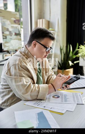 A young man with Down syndrome works on his smartphone at his desk. Stock Photo