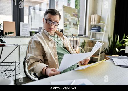 A young man with Down syndrome sits at his desk, reviewing documents. Stock Photo