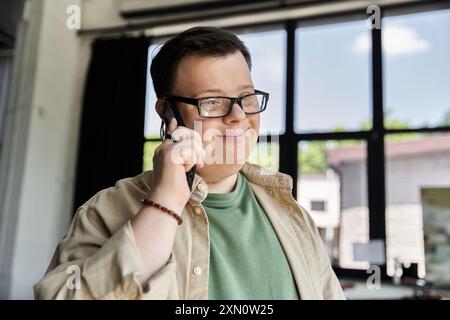 A young man with Down syndrome smiles while talking on a cell phone. Stock Photo
