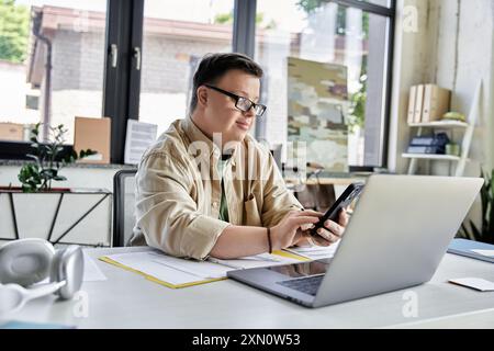 Young man with Down syndrome uses smartphone with open laptop Stock Photo