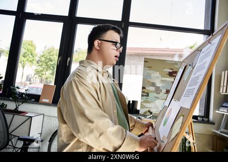 A young man with Down syndrome stands beside a presentation board, confidently sharing his ideas. Stock Photo