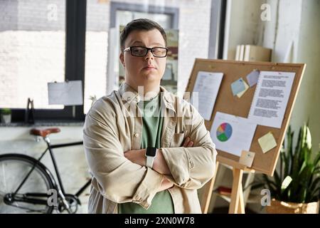Confident young man with Down syndrome in office, arms crossed, facing camera Stock Photo