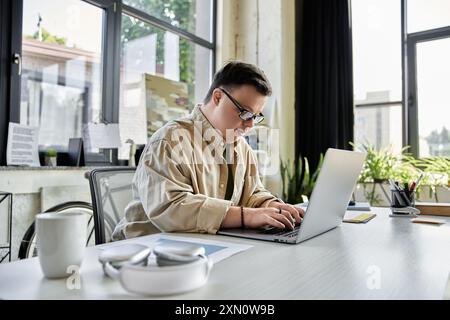 A young man with Down syndrome works on a laptop at a desk. Stock Photo