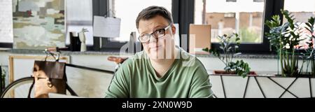 Young man with Down syndrome smiles at camera in room with bicycle and plants Stock Photo