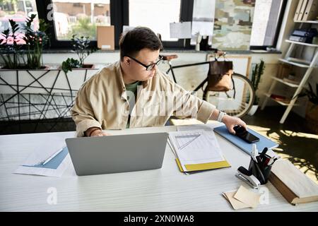 A young man with Down syndrome sits at a desk in an office, working on a laptop. Stock Photo