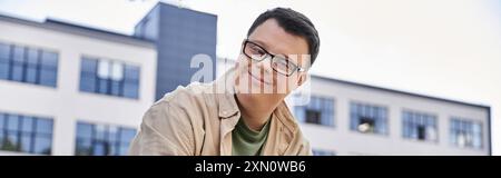 A man with Down syndrome smiles as he walks past a building. Stock Photo