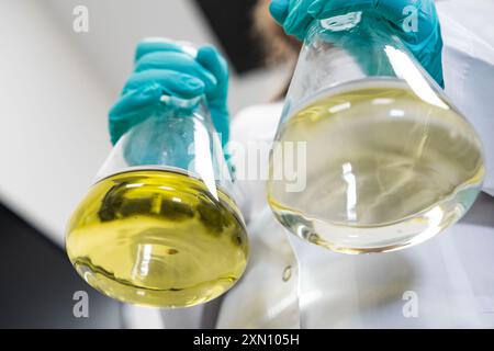 Chemist in lab coat and rubber gloves vigorously shaking yellow samples before analysis Stock Photo