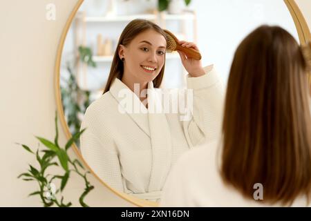 Beautiful woman brushing hair near mirror in bathroom Stock Photo