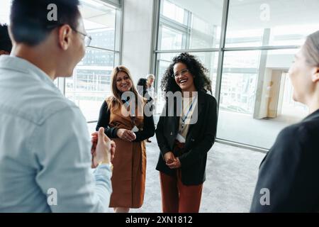 Group of colleagues engaging in networking at a corporate event, sharing laughter and socializing in a modern office environment. Stock Photo