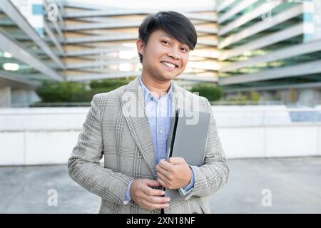 Young Man in Gray Suit Holding Laptop Outside Modern Building Stock Photo