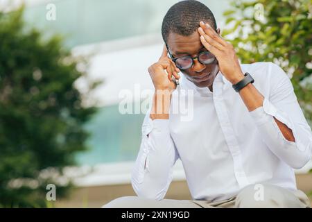 Man Wearing Glasses Talking on Phone, Holding Head in Hand Stock Photo