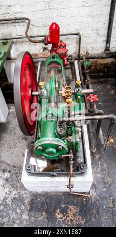An old industrial machine with a red spinning wheel and various metal pipes and valves in a factory setting. Stock Photo